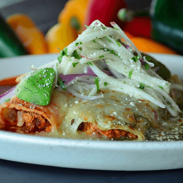 Close-up of Neon Cactus enchiladas topped with avocado, radish, red onion, and cilantro.