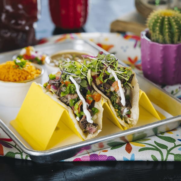 Two steak tacos with microgreens and crema, served with rice and salsa on a metal tray.