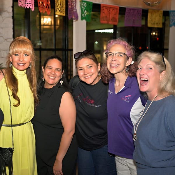 Five smiling women posing together under colorful Mexican papel picado decorations at Neon Cactus.