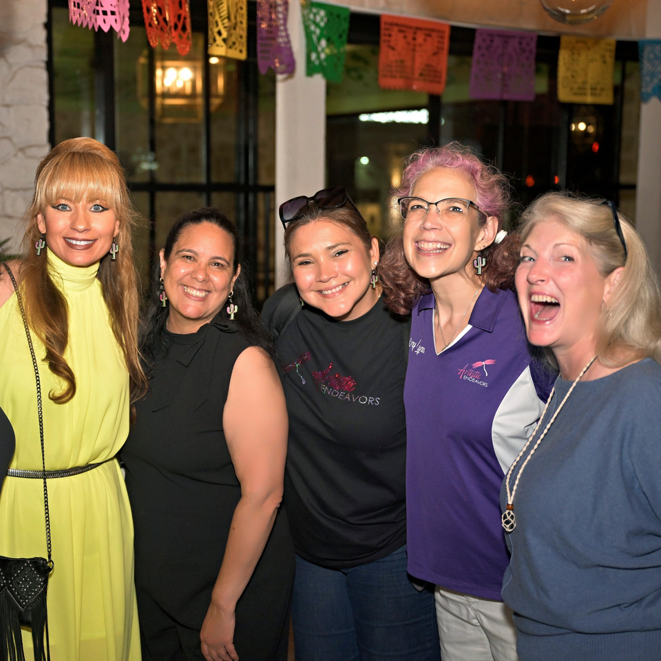 Five smiling women posing together under colorful Mexican papel picado decorations at Neon Cactus.