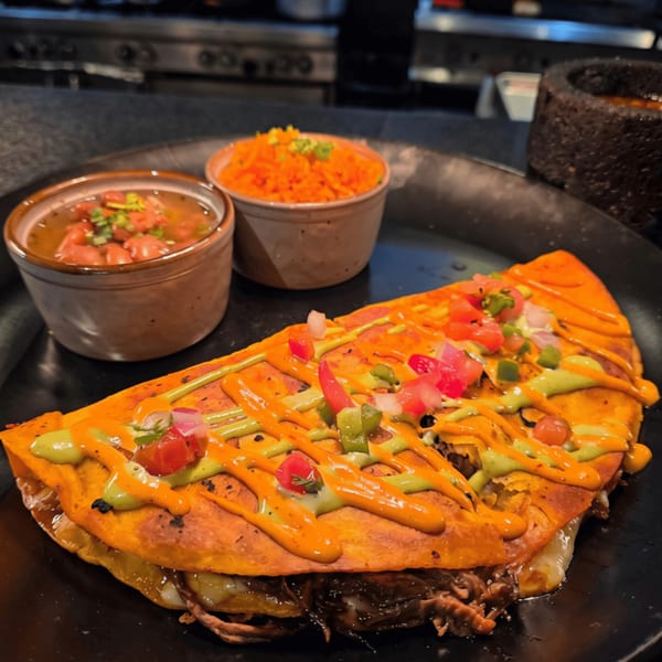 A large quesadilla with sauces and toppings, served with sides of beans and rice.