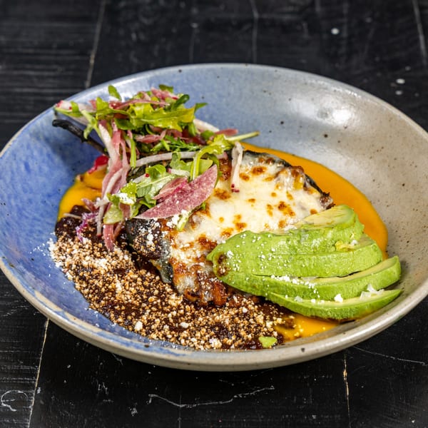 A Mexican dish with a cheese-covered poblano pepper, avocado, and salad in a blue bowl.