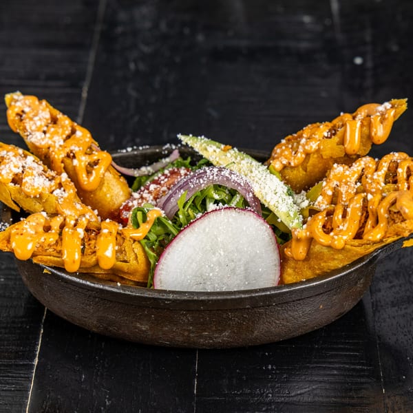 Mexican dish with crispy golden tacos drizzled with orange sauce, cheese, and fresh vegetables.