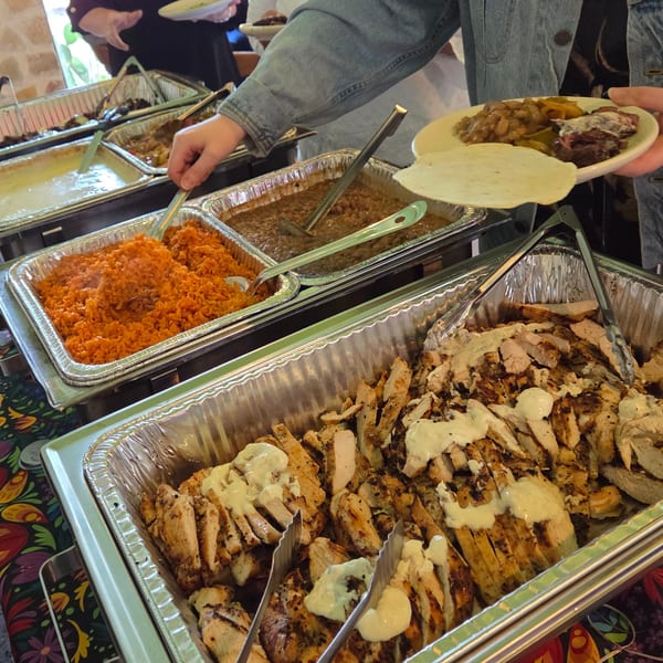 A person serving themselves from a Mexican food buffet with rice, beans, and sliced chicken.