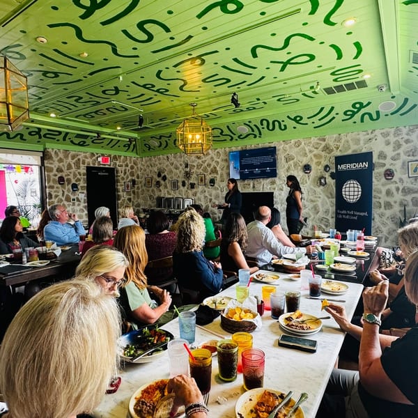 People seated at tables with food and drinks, listening to a presentation in a vibrant Mexican restaurant.