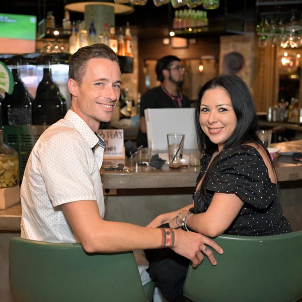 A smiling man and woman sit at a bar in Neon Cactus, with a bartender in the background.