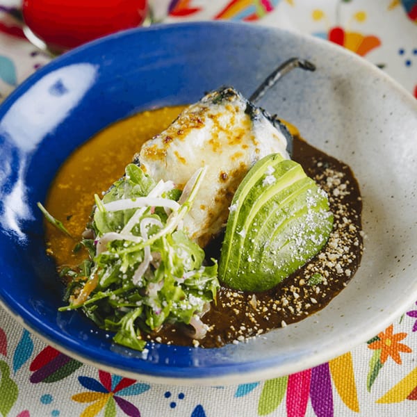 A Mexican chile relleno dish with cheese, avocado, and greens in a blue bowl.