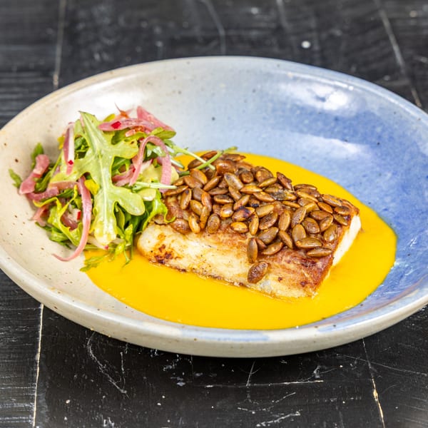 Mexican fish dish with pumpkin seeds, yellow sauce, and a side salad on a blue and white plate.