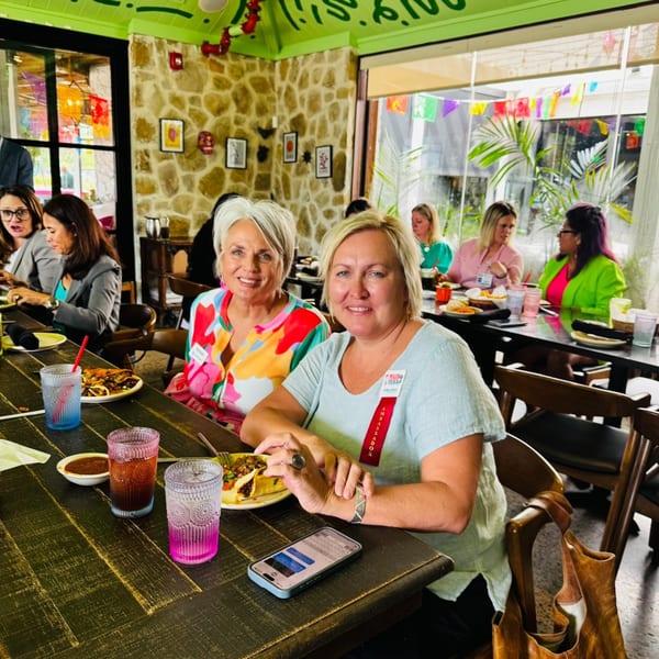 Two women smiling at the camera, seated at a table with food and drinks at Neon Cactus.