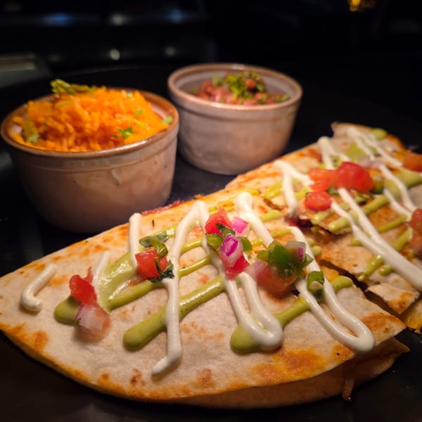 Quesadillas drizzled with sour cream and guacamole, served with orange rice and beans.