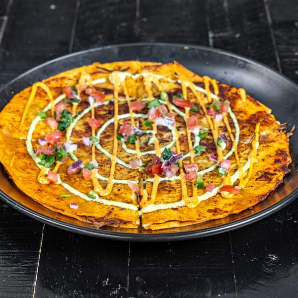 A Neon Cactus quesadilla topped with pico de gallo, green and orange sauces on a black plate.