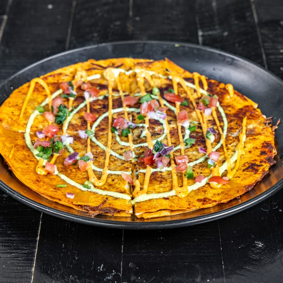 A Neon Cactus quesadilla topped with pico de gallo, green and orange sauces on a black plate.
