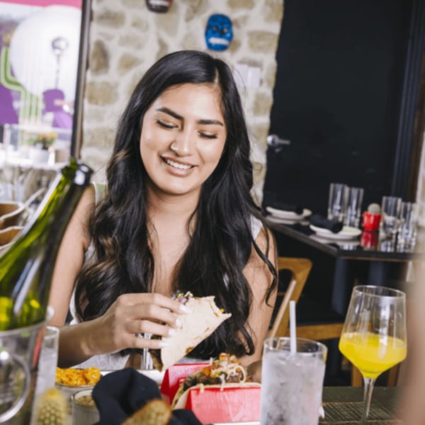 Smiling woman enjoying a taco at Neon Cactus, with drinks and Mexican decor in the background.