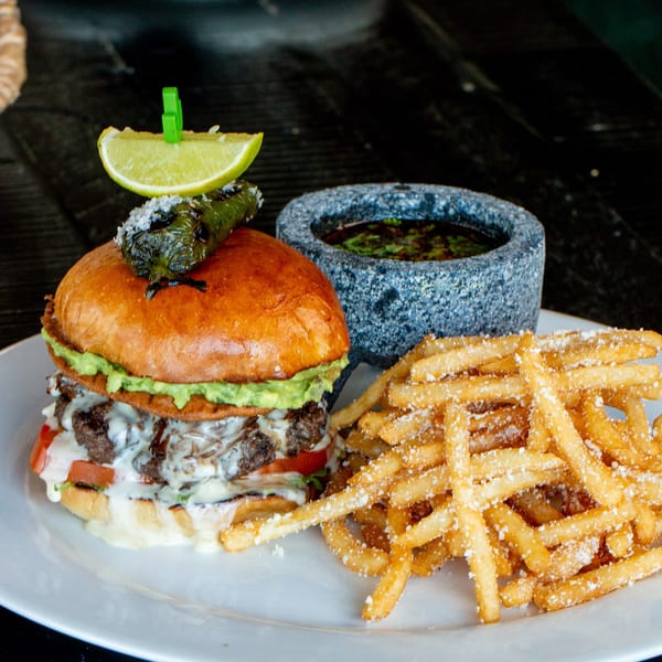 Gourmet burger with guacamole, cheese, and a grilled pepper, served with parmesan fries and dipping sauce.