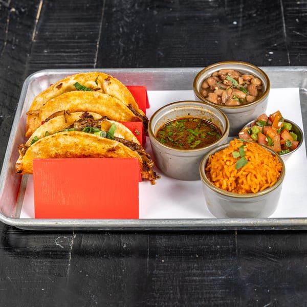Crispy birria tacos with dipping sauce, rice, beans, and pico de gallo on a metal tray.