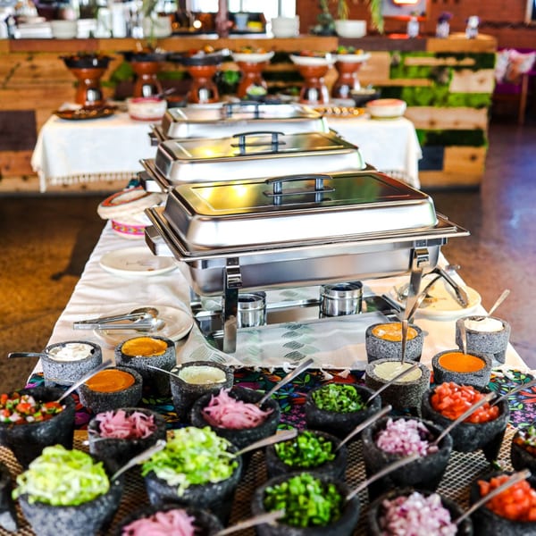 A Mexican buffet with chafing dishes and many small bowls of colorful toppings and sauces.