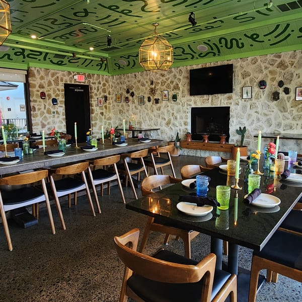 Neon Cactus dining room with long tables set with candles, colorful glasses, and a vibrant green ceiling.