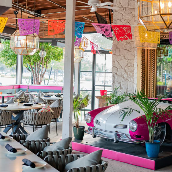 Neon Cactus restaurant interior with colorful papel picado, dining tables, and a pink and white vintage car.